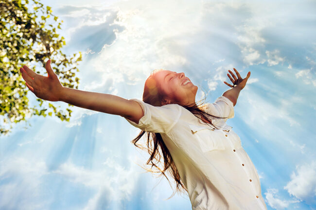 Young woman raising her arms and enjoys sunny day
